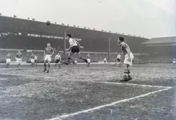 John Groves leaps to send a header across the penalty area. Tommy Docherty stands and stares