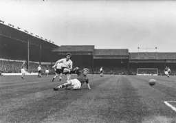 A defender slides in but cannot prevent Billy Bingham taking a shot at goal