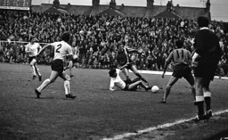 Peter Cruse attempts to win the ball watched by John Aston