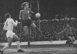 The ball misses Ron Futcher but goes to the waiting John Aston