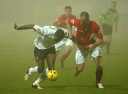 Enoch Showunmi powers forward head down with the ball challenged by a Crewe player