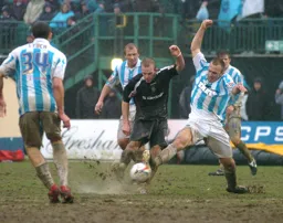 Rowan Vine strikes the ball through a pool of water whilst challenged by a Brighton player