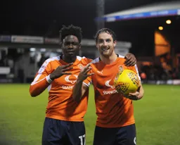 Danny Hylton celebrates his hat-trick with the match ball. Pelly-Ruddock Mpanzu shares the moment