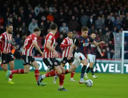 Reece Burke drives forward with the ball, followed by a cohort of Sheffield United players