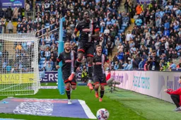 Elijah Adebayo leaps for joy after scoring the second goal. Carlton Morris and Tom Krauss run to join in.